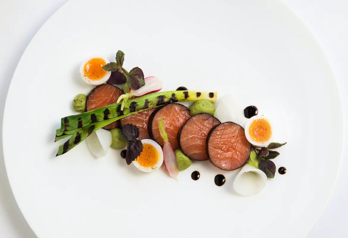 Plated starter with sliced meat, quail eggs and grilled leeks on a white plate