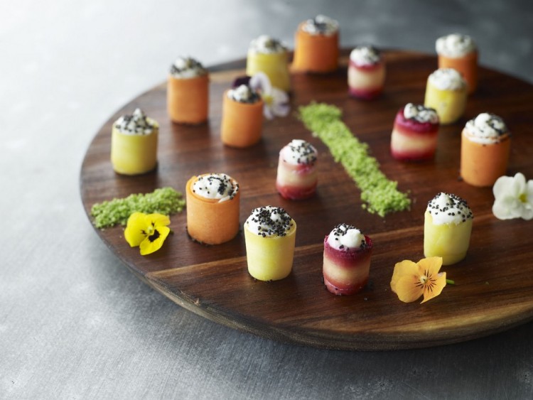 Colourful canapés served on a round wooden board with edible flowers