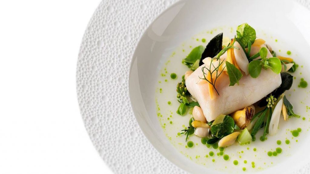 Filet de poissons dans une assiette creuse avec fleur et pousse de salade verte et jaune